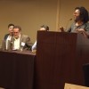 Person speaking at a podium next to three seated panelists