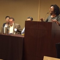 Person speaking at a podium next to three seated panelists