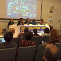 Five panelists and two rows of the audience with a projection screen in the back behind panelists